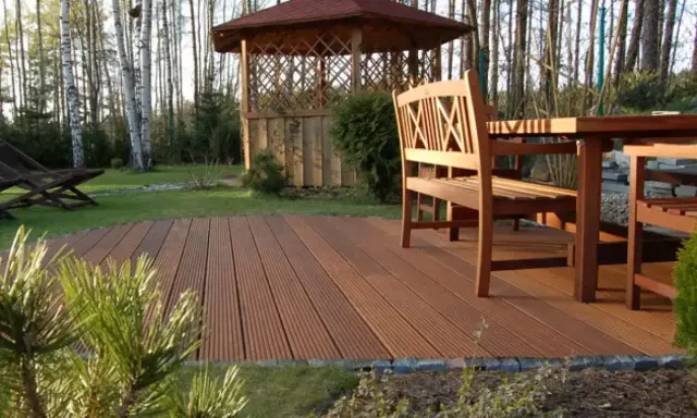 Drewniany taras z meblami i altaną w ogrodzie. Świetny pomysł na tani taras, który doda uroku Twojej przestrzeni.