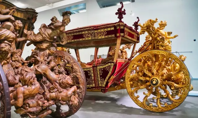 Prunkvolle Kutschen im Kutschenmuseum Lissabon: Eine aus Holz geschnitzte, die andere golden verziert, beide mit aufwendigen Figuren.