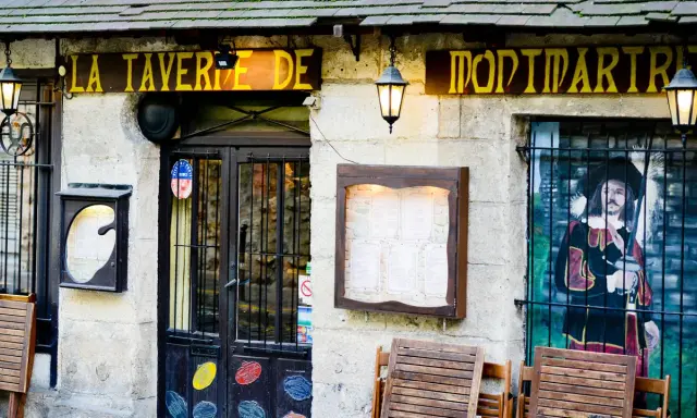 La taverne de Montmartre, une définition de l'ambiance parisienne. Façade de pierre, enseigne jaune, menu affiché, et une peinture murale d'un mousquetaire.