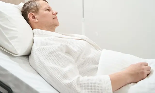 Mężczyzna w białym szlafroku leży w szpitalnym łóżku, przygotowując się do usunięcia pęcherza moczowego.