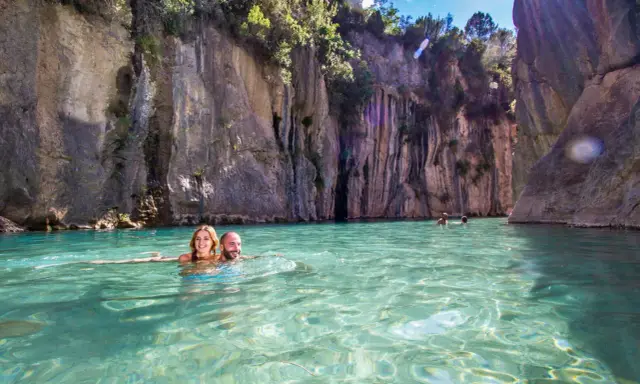 Pareja nadando en aguas cristalinas rodeados de acantilados. ¡Una gran idea de qué hacer en Castellón con niños!