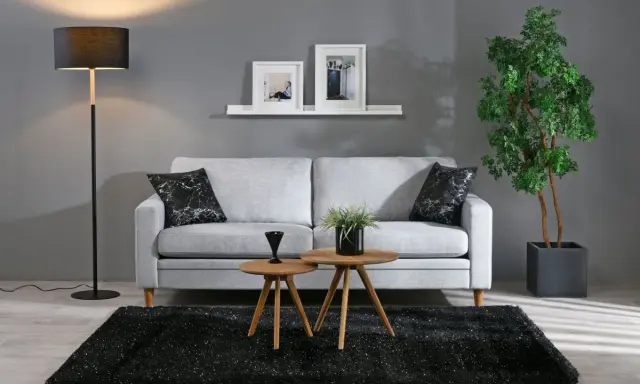En stilren inredning grått med en ljusgrå soffa, svart matta och en golvlampa. Två runda bord framför soffan.