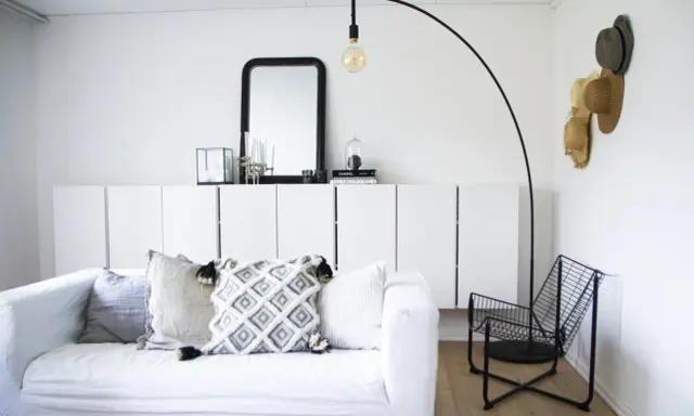 En stilren och modern manlig inredning med vit soffa, svarta detaljer och en golvlampa.