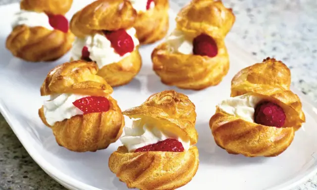 Små petit choux fyllda med vispgrädde och toppade med hallon eller jordgubbar. En härlig dessert!