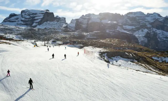 Narciarze szusują po ośnieżonym stoku w Dolomitach. Idealne miejsce, gdzie na narty we Włoszech, z majestatycznymi górami w tle.