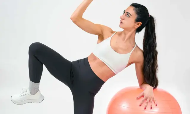 Frau macht Übungen mit Gymnastikball. Sie fragt sich, was ist Kreatin, während sie ihre Muskeln trainiert.