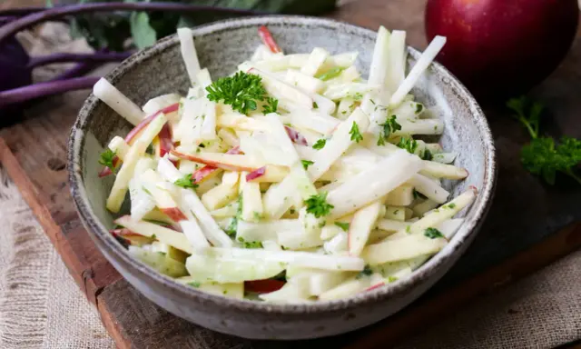 Kohlrabi Salat mit Apfelstücken und frischer Petersilie, garniert mit einem roten Apfel im Hintergrund.