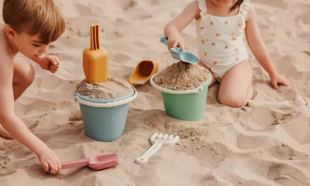 Niños disfrutando de juegos en la playa con cubos y palas de arena.
