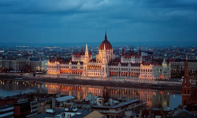 Budynek Parlamentu w Budapeszcie nocą, odbijający się w Dunaju. Miasto tętni życiem, aspirując do miana najbardziej imprezowych miast w Europie.