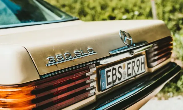 Detalle de un Mercedes 350 SLC dorado, con la luz de matrícula visible, listo para pasar la ITV.