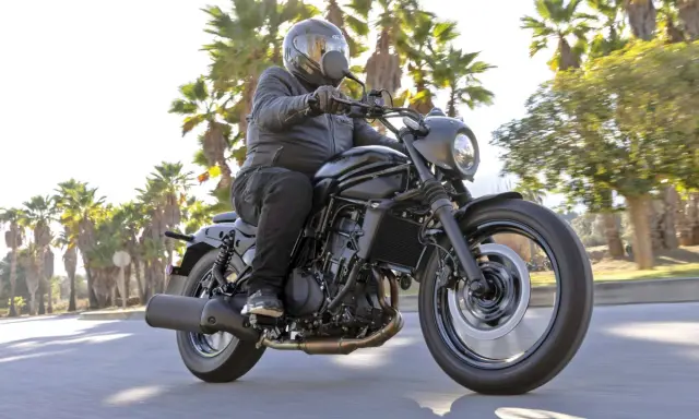 Mężczyzna w kasku jedzie czarnym motocyklem Kawasaki EN 500. Wady i zalety tego modelu są dyskutowane podczas jazdy wśród palm.