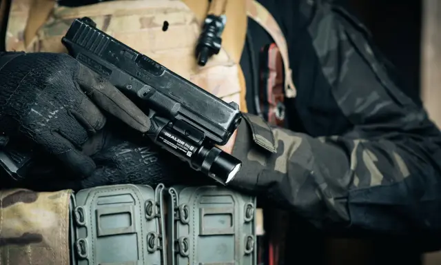 Dłoń w rękawiczce trzyma pistolet z zamontowanym na szynie taktycznym laserem do broni.