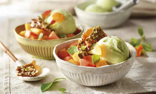 Deliciosos postres saludables: helado verde cremoso con trozos de melón, papaya y un toque crujiente de pistachos.