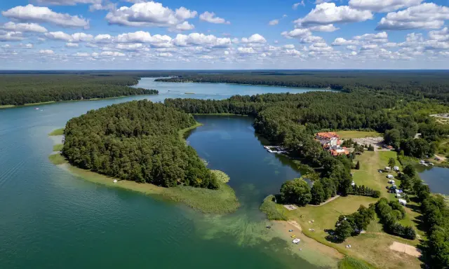 Malownicze jezioro Urszulewskie otoczone lasem, z hotelem i polem namiotowym na brzegu.