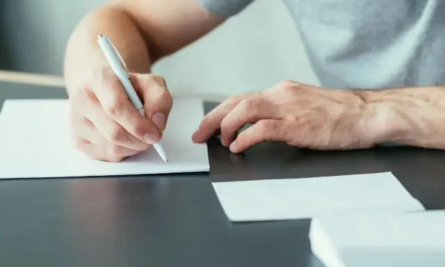 Mężczyzna pisze ręcznie list motywacyjny, przygotowując się do ważnego spotkania.