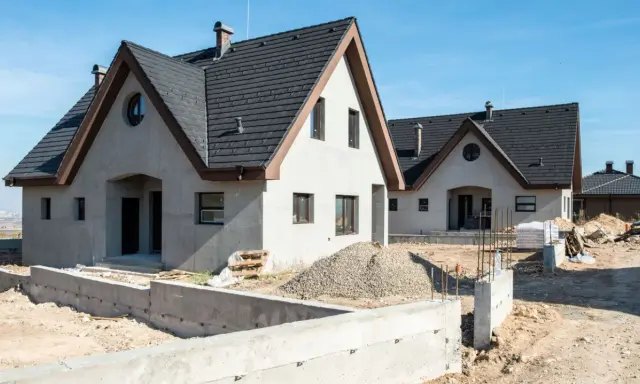 Nowe budynki usługowe z częścią mieszkalną w trakcie budowy. Widać fundamenty, materiały budowlane i dachy.