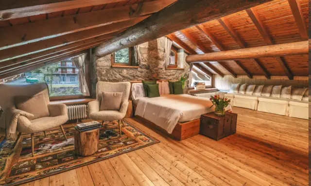Accogliente camera con camino, travi in legno a vista, letto comodo, poltrone soffici e un tappeto decorato.
