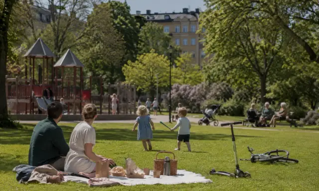 Familj picknickar i parken medan barnen leker. En perfekt dag för aktiviteter i Lund för vuxna och barn.