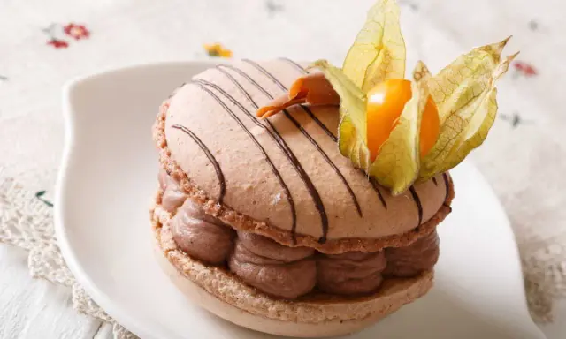 Un macaron chocolat au lait, garni de crème onctueuse et décoré d'une physalis, prêt à être dégusté.