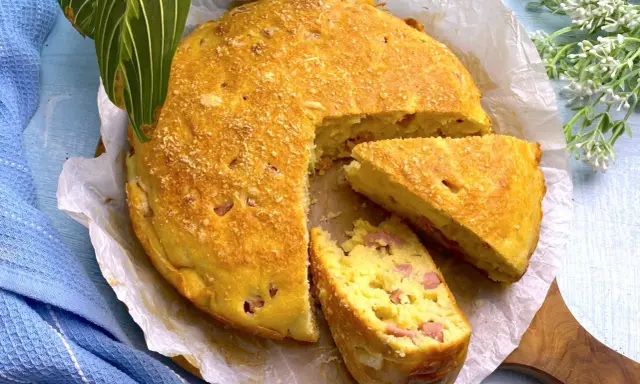 Una deliziosa torta salata prosciutto e formaggio, dorata e soffice, con una fetta tagliata per mostrare il ripieno.