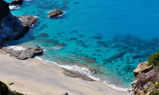 Spiaggia dorata e mare cristallino con scogli a Capo Cozzo.