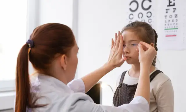 Okulista wykonuje ćwiczenia na akomodację oka u dziewczynki, zasłaniając jej jedno oko.