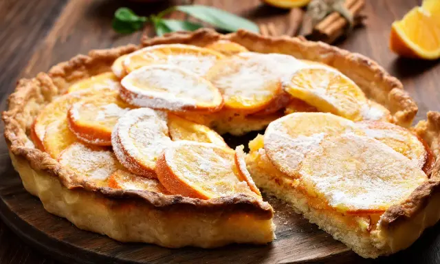 Une délicieuse tarte à l'orange, garnie de fines tranches d'agrumes et saupoudrée de sucre glace, sur un fond de bois rustique.