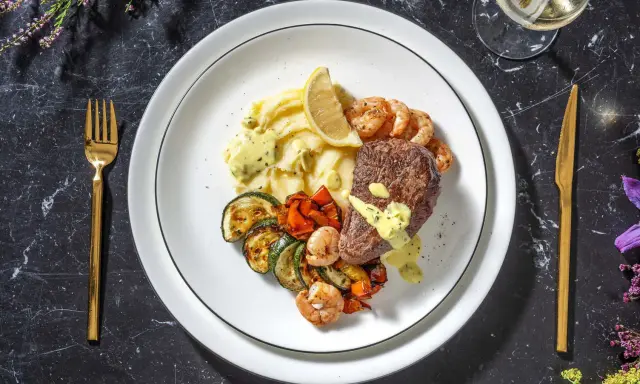 Ein köstliches Surf and Turf Rezept: saftiges Steak, Garnelen, Kartoffelpüree und gegrilltes Gemüse auf einem Teller.