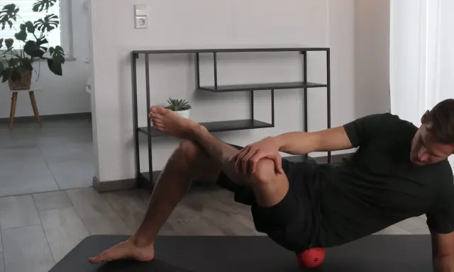 Mann dehnt den Piriformis mit einem roten Ball unter der Hüfte.