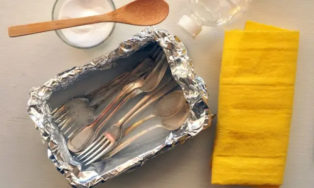 Czyszczenie sztućców sodą: folia aluminiowa, soda, woda i żółta ściereczka.