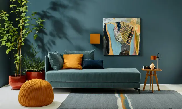 Ein Wohnzimmer mit einem türkisfarbenen Sofa, orangefarbenen Akzenten und einem abstrakten Gemälde. Die Wandfarbe könnte die Farbe des Jahres 2026 sein.