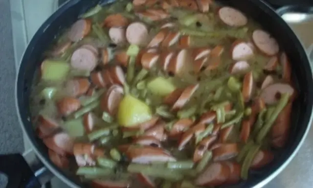 Ein deftiges schnippelbohnen rezept mit Kartoffeln und Würstchen in einer Pfanne.