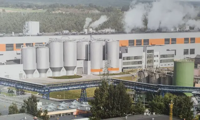 Ogromna fabryka celulozy w Polsce z wieloma silosami i rurociągami, z której unosi się para.
