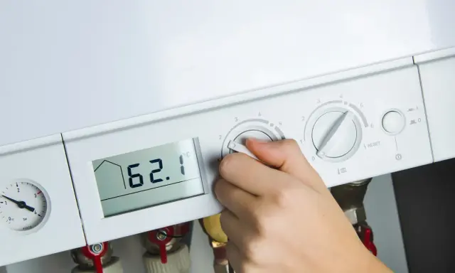 Dłoń reguluje ustawienie pieca gazowego. Na wyświetlaczu 62.1°C, obok manometr i pokrętła regulacji.