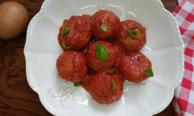 Pallotte cacio e ova in salsa di pomodoro, guarnite con basilico fresco. Un uovo intero è visibile a sinistra.