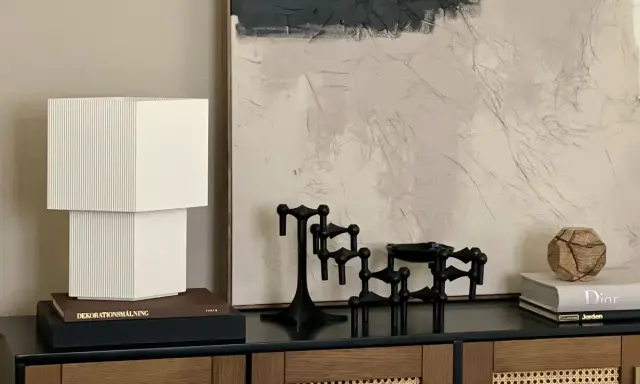 En stilren stilleben inredning med en vit lampa, svarta ljusstakar och en bok med texten "Dior".