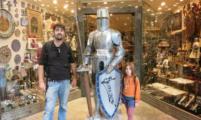 Un padre y su hija posan junto a una armadura de caballero en una tienda de souvenirs en Toledo con niños.