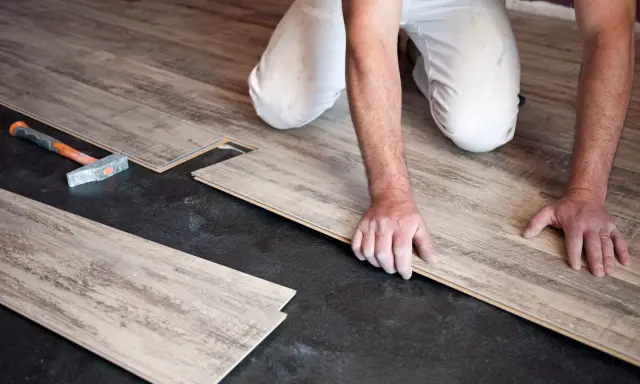 Pose de parquet flottant : un artisan installe des lames de bois sur un sol noir. Le prix de pose est une préoccupation pour ce type de revêtement.
