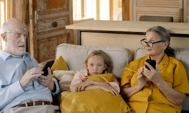 Abuela paterna celosa mira con recelo mientras el abuelo y la nieta están absortos en sus teléfonos.