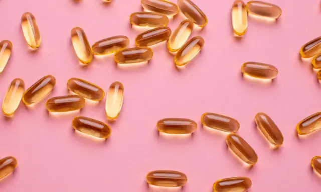 Capsule dorate sparse su sfondo rosa, utili per la vitamina D in gravidanza.