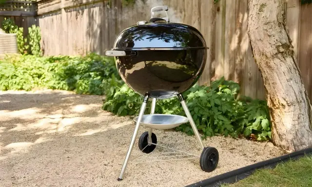 Un barbecue noir fumant, prêt à faire griller de bonnes choses dans le jardin. L'été arrive, il est temps de faire un barbecue !