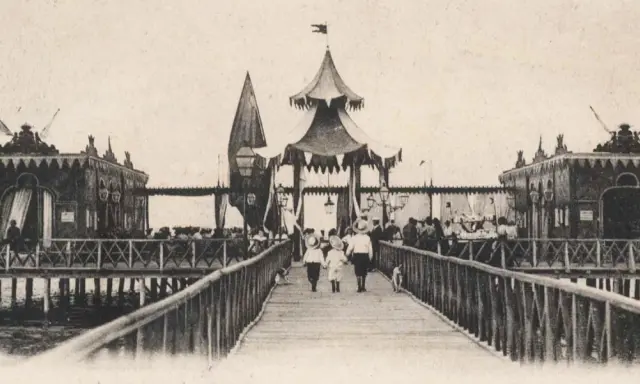 Antica passeggiata sui bagni isola di Cervia, con bambini che camminano sul pontile verso le strutture sul mare.