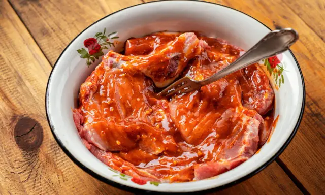 Morceaux de viande crue dans une sauce rouge épicée, prêts à être cuisinés. Une fourchette est plantée dans la préparation.