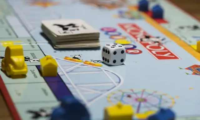 Kostka i pionki na planszy Monopoly. Gra planszowa uczy strategii, negocjacji i zarządzania finansami, realizując cele i zadania.