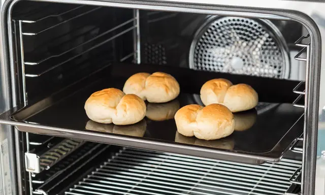 Cinq petits pains dorés sur une plaque de cuisson dans un four. C'est une bonne question : qu'est-ce qu'un lèchefrite ? C'est cette plaque !