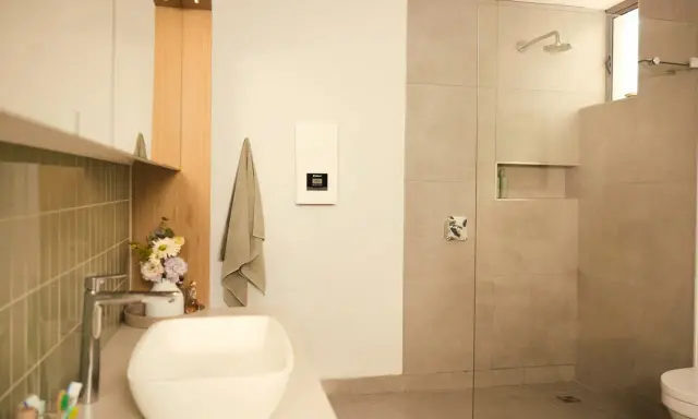 Modernes Bad mit Dusche und Waschbecken. Ein Durchlauferhitzer hängt an der Wand, der für warmes Wasser sorgt, auch wenn man ihn an 230V anschließen möchte.