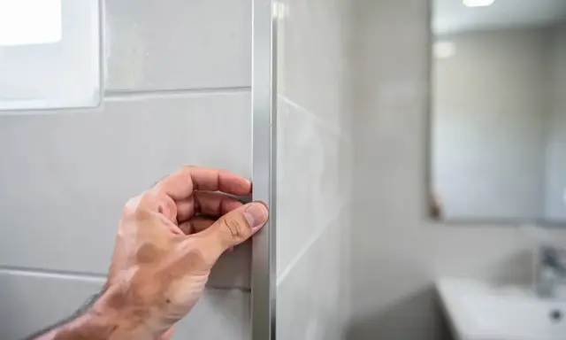 Main tenant vérifie le joint en L d'un profilé de finition sur un mur carrelé.