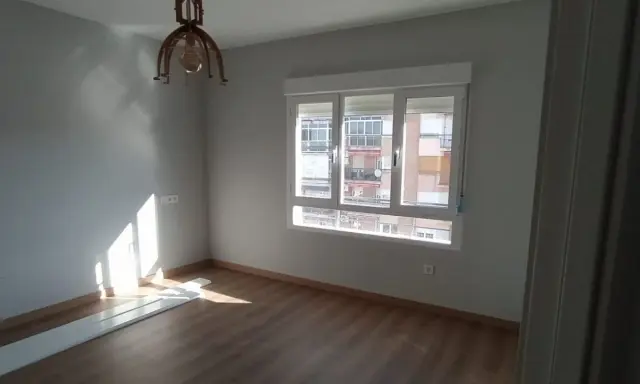 Habitación con suelo de madera, paredes grises y ventana. El sol ilumina la estancia, sugiriendo un buen **precio medio reforma integral**.