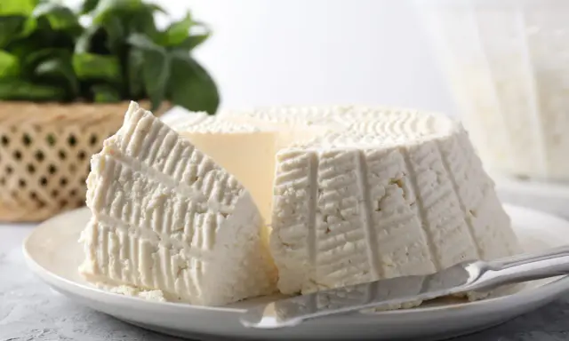 Un morceau de ricotta fraîche sur une assiette, avec des herbes en arrière-plan. Idéal pour connaître les calories de la ricotta.