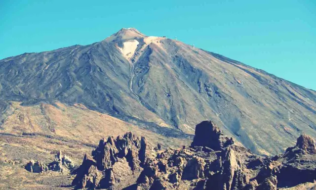 Vulkan Pico del Teide mit felsiger Landschaft im Vordergrund und blauem Himmel.